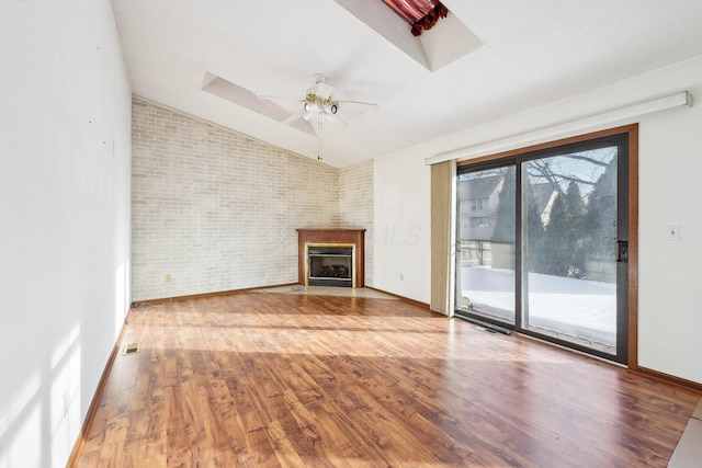 unfurnished living room with brick wall, lofted ceiling, wood-type flooring, a large fireplace, and ceiling fan