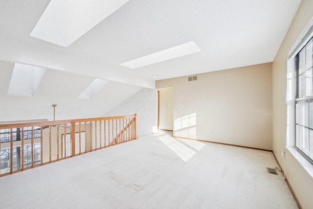 spare room with a wealth of natural light, lofted ceiling with skylight, and light colored carpet