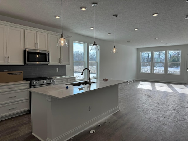 kitchen with decorative light fixtures, white cabinetry, sink, stainless steel appliances, and a center island with sink