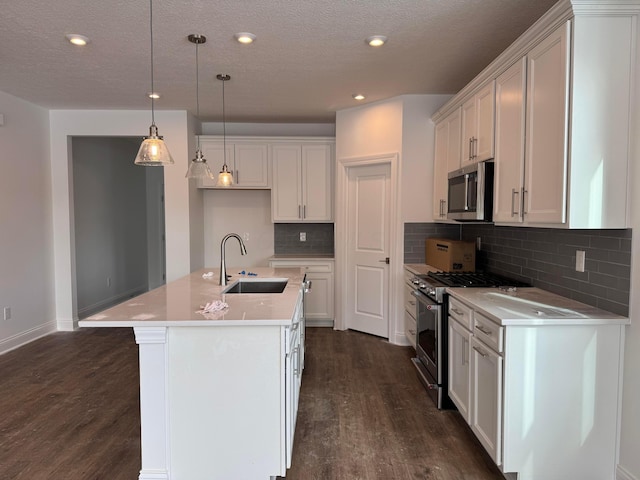 kitchen with sink, appliances with stainless steel finishes, white cabinets, a center island with sink, and decorative light fixtures