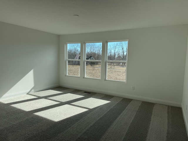 unfurnished room featuring dark carpet, visible vents, plenty of natural light, and baseboards