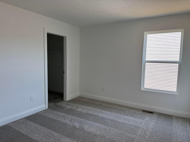 carpeted empty room with baseboards, visible vents, and a textured ceiling