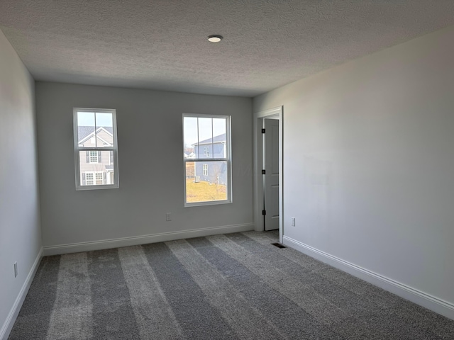 carpeted spare room with plenty of natural light, visible vents, baseboards, and a textured ceiling