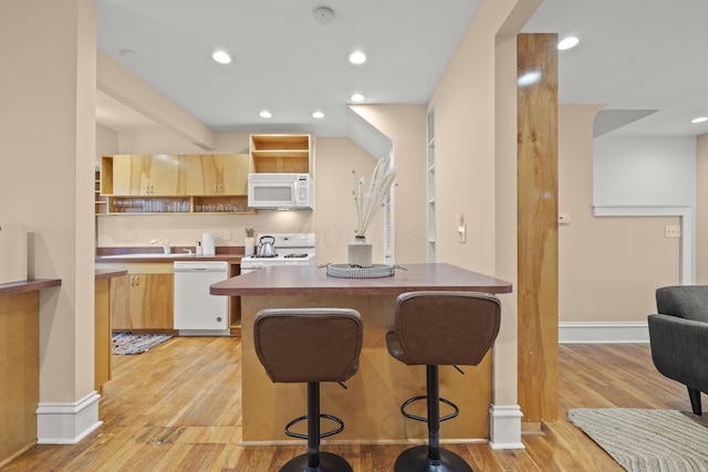 kitchen featuring white appliances, a kitchen breakfast bar, light hardwood / wood-style floors, and light brown cabinets