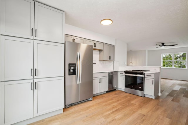 kitchen with appliances with stainless steel finishes, kitchen peninsula, light hardwood / wood-style floors, and decorative backsplash