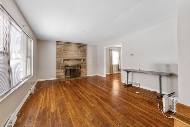 unfurnished living room featuring dark wood-type flooring, a fireplace, and an AC wall unit