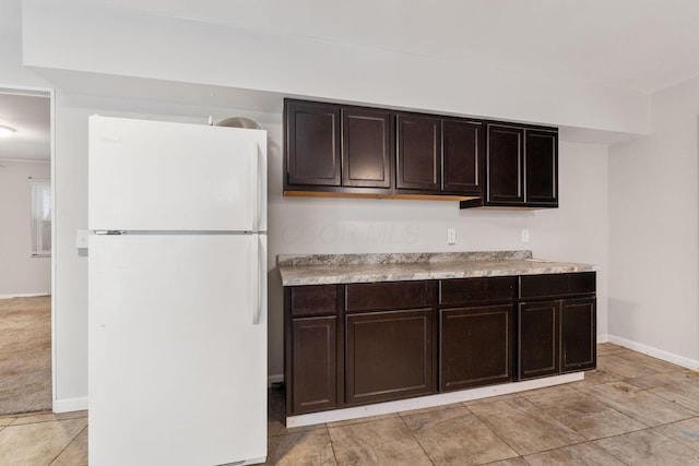 kitchen featuring light colored carpet, dark brown cabinetry, and white fridge