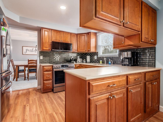 kitchen with sink, decorative backsplash, light hardwood / wood-style floors, kitchen peninsula, and stainless steel appliances