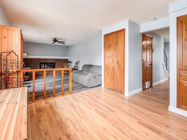 living room with ceiling fan, a textured ceiling, a fireplace, and light hardwood / wood-style flooring