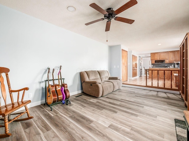 living room with ceiling fan, a textured ceiling, and light hardwood / wood-style floors