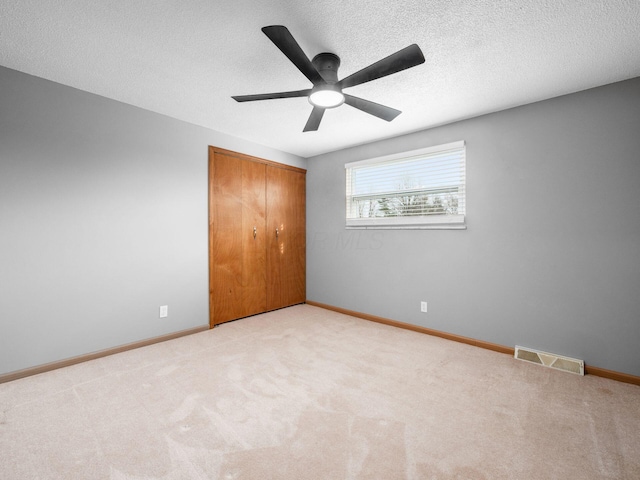 unfurnished bedroom featuring ceiling fan, light colored carpet, a textured ceiling, and a closet