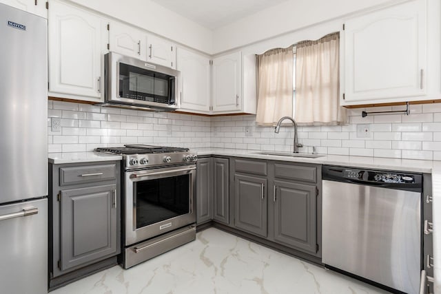 kitchen with sink, appliances with stainless steel finishes, gray cabinetry, white cabinetry, and backsplash