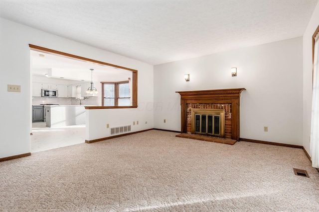 unfurnished living room featuring sink, an inviting chandelier, a brick fireplace, light carpet, and a textured ceiling