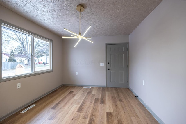 unfurnished dining area with a textured ceiling, light hardwood / wood-style flooring, and an inviting chandelier