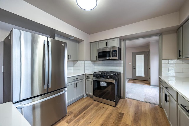 kitchen with gray cabinets, light hardwood / wood-style flooring, stainless steel appliances, and tasteful backsplash