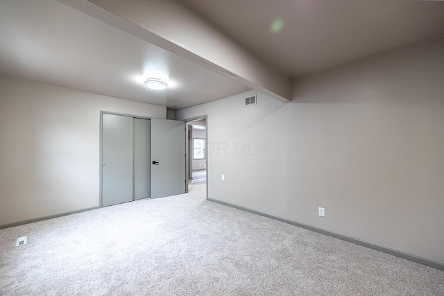 unfurnished bedroom with carpet, a closet, and beamed ceiling