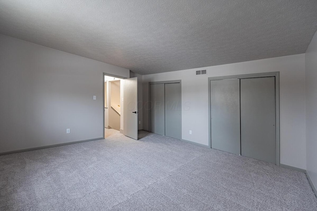 unfurnished bedroom with multiple closets, light colored carpet, and a textured ceiling