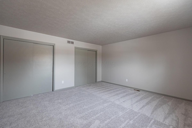 unfurnished bedroom featuring carpet flooring, a textured ceiling, and two closets