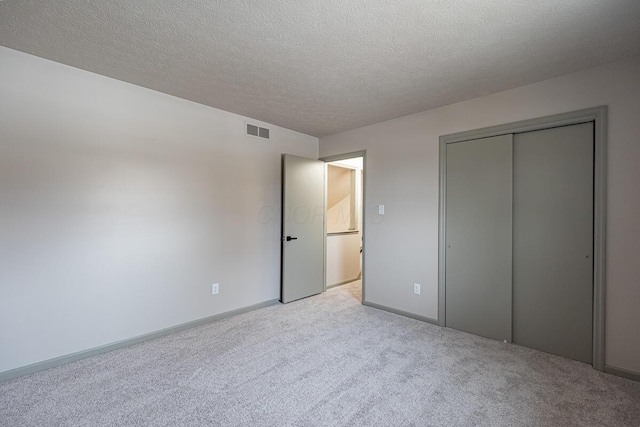 unfurnished bedroom featuring light carpet, a textured ceiling, and a closet