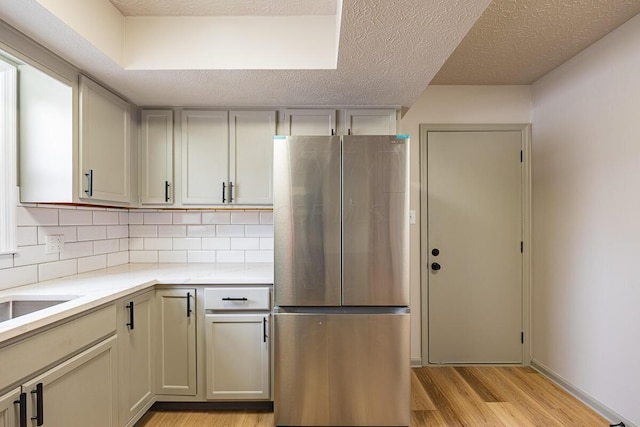 kitchen featuring sink, a textured ceiling, stainless steel fridge, light hardwood / wood-style floors, and decorative backsplash