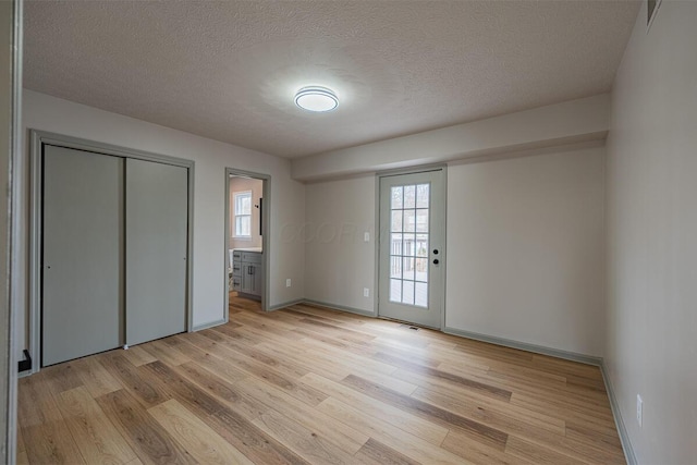 unfurnished bedroom with a closet, light hardwood / wood-style flooring, a textured ceiling, and ensuite bath