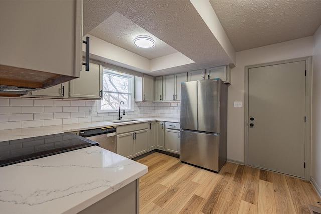 kitchen with sink, appliances with stainless steel finishes, tasteful backsplash, light stone counters, and a textured ceiling