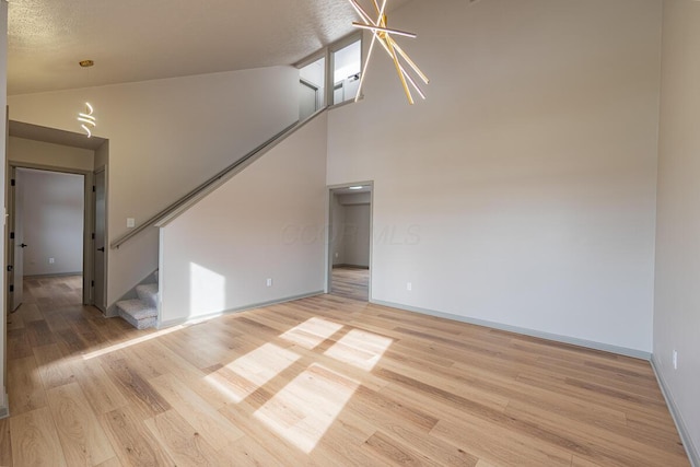 unfurnished living room featuring high vaulted ceiling, a textured ceiling, and light wood-type flooring