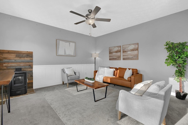 carpeted living room featuring a wood stove and ceiling fan