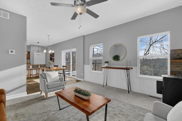 carpeted living room featuring ceiling fan with notable chandelier