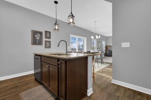 kitchen featuring light stone countertops, a kitchen island with sink, sink, and decorative light fixtures