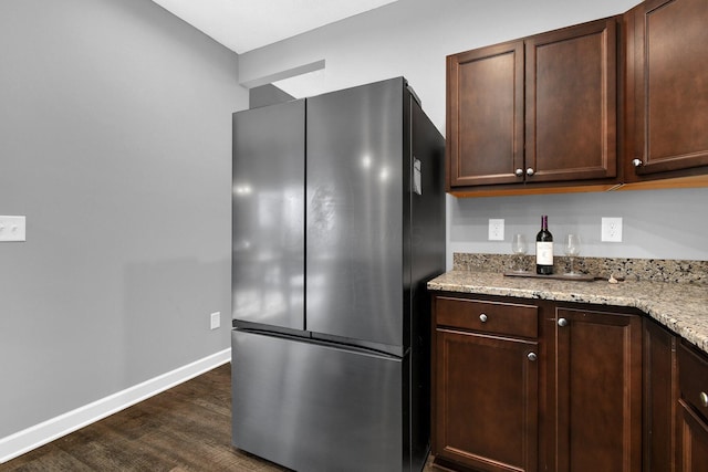 kitchen with dark brown cabinets, stainless steel fridge, light stone countertops, and dark hardwood / wood-style floors