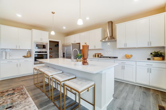 kitchen with decorative light fixtures, appliances with stainless steel finishes, white cabinets, wall chimney range hood, and backsplash