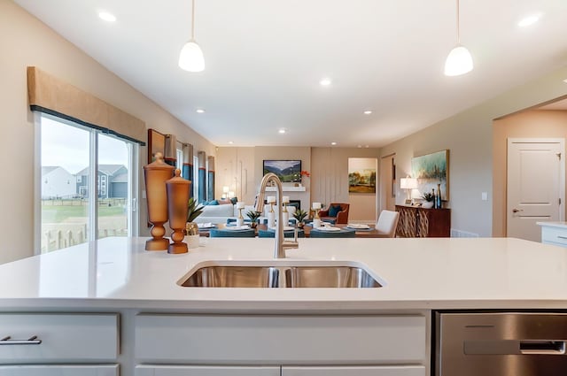 kitchen featuring hanging light fixtures, an island with sink, sink, and white cabinetry