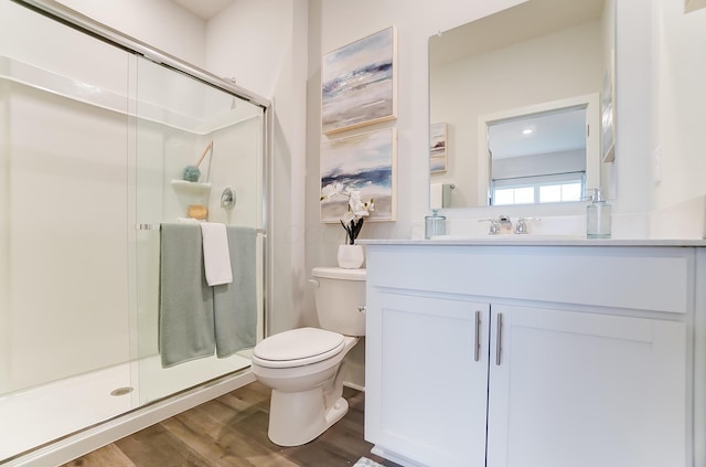 bathroom featuring wood-type flooring, toilet, a shower with shower door, and vanity