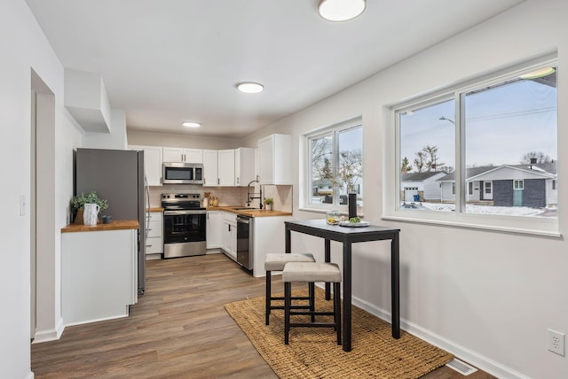 kitchen with sink, appliances with stainless steel finishes, white cabinetry, backsplash, and wood-type flooring