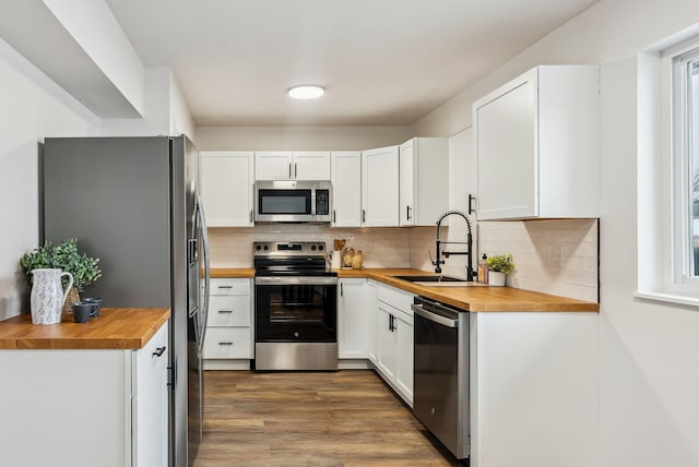 kitchen featuring butcher block countertops, sink, white cabinetry, stainless steel appliances, and decorative backsplash