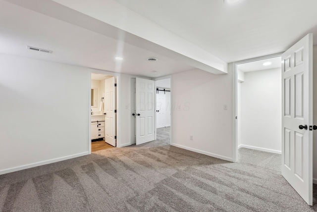 unfurnished bedroom with a barn door, connected bathroom, and light colored carpet