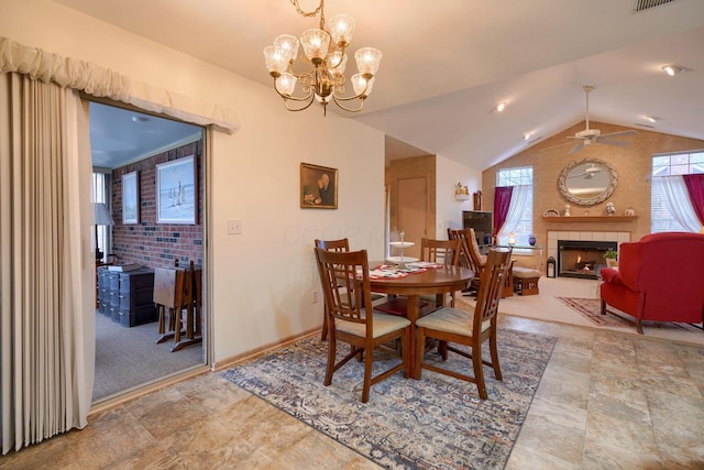 dining space featuring lofted ceiling, a tiled fireplace, and ceiling fan with notable chandelier