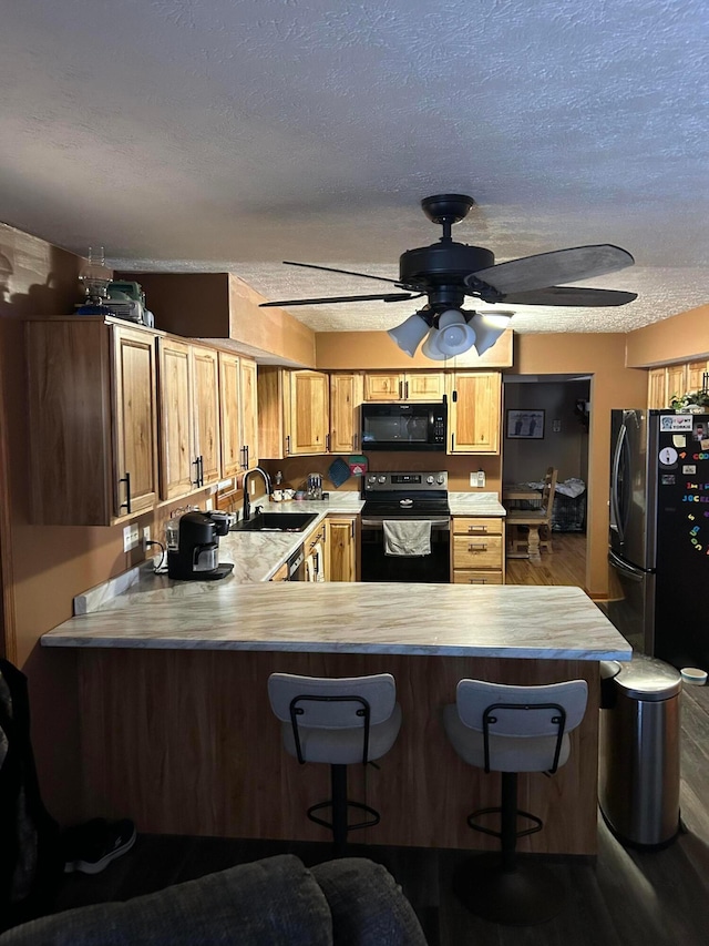 kitchen with sink, wood-type flooring, black appliances, a kitchen bar, and kitchen peninsula