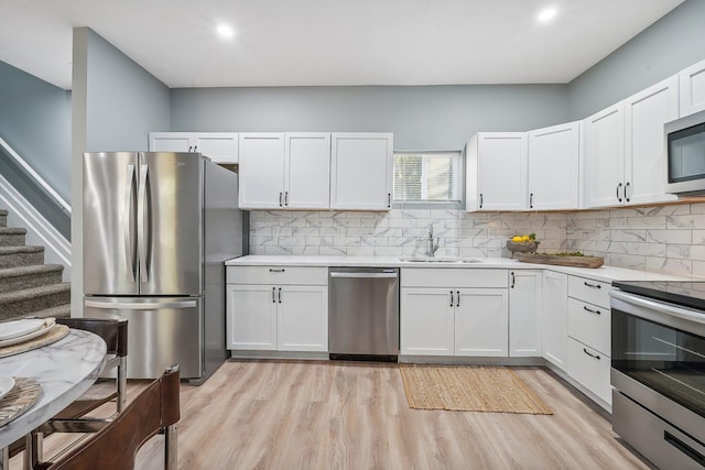 kitchen with sink, tasteful backsplash, light wood-type flooring, appliances with stainless steel finishes, and white cabinets