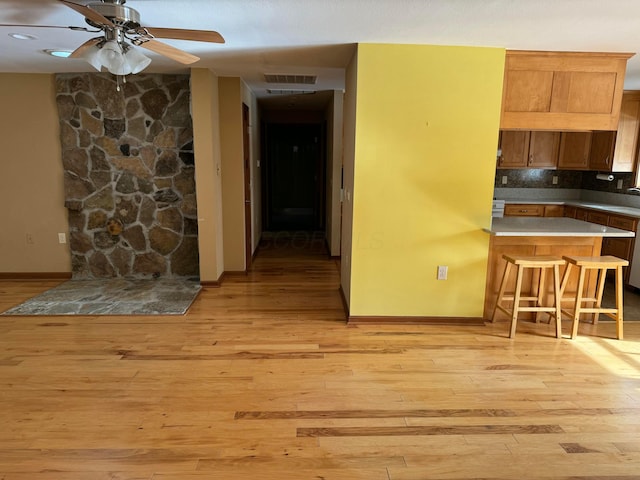 kitchen featuring light hardwood / wood-style flooring, ceiling fan, backsplash, a kitchen bar, and kitchen peninsula