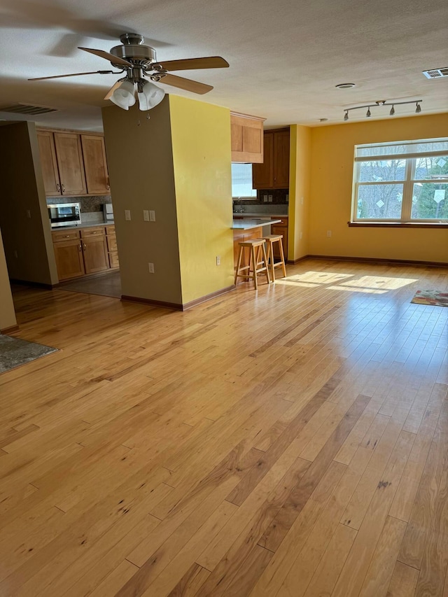 unfurnished living room featuring light hardwood / wood-style flooring, ceiling fan, and track lighting