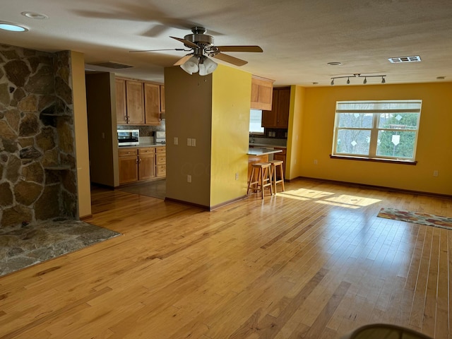 unfurnished living room with a textured ceiling, a fireplace, ceiling fan, and light hardwood / wood-style flooring