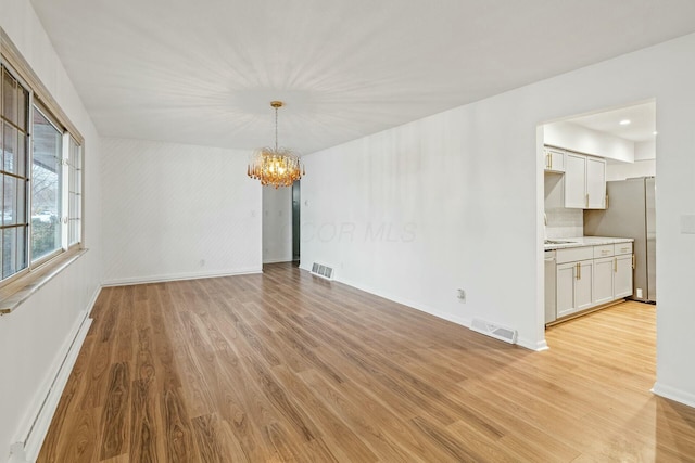 empty room featuring baseboard heating, a notable chandelier, and light wood-type flooring