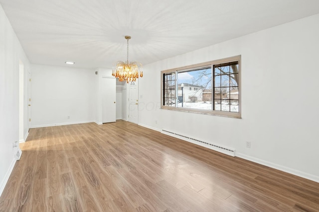 empty room with baseboard heating, an inviting chandelier, and light hardwood / wood-style floors