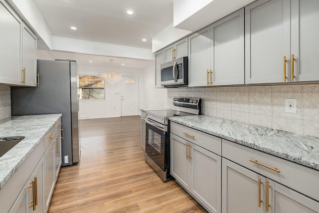 kitchen with appliances with stainless steel finishes, tasteful backsplash, gray cabinetry, light stone counters, and light wood-type flooring