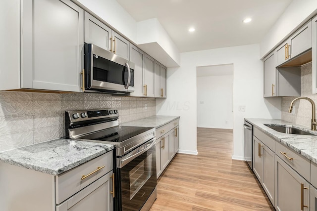 kitchen with gray cabinets, sink, stainless steel appliances, light stone countertops, and light hardwood / wood-style flooring