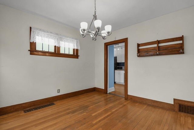 empty room featuring a notable chandelier and hardwood / wood-style flooring