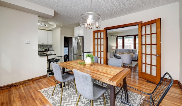 dining room with an inviting chandelier, light hardwood / wood-style floors, a textured ceiling, and french doors