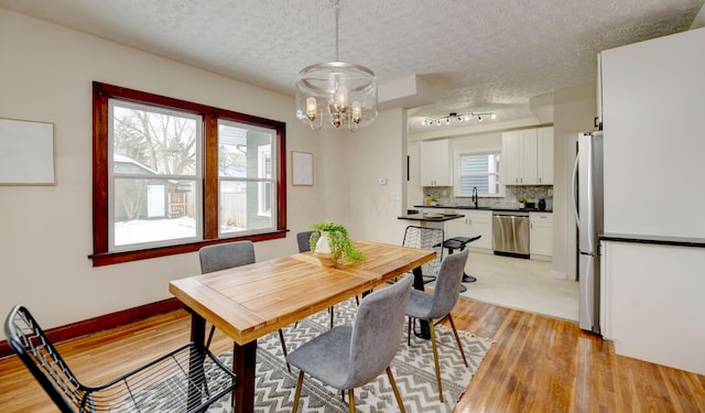 dining space featuring sink, a notable chandelier, light hardwood / wood-style flooring, and a textured ceiling